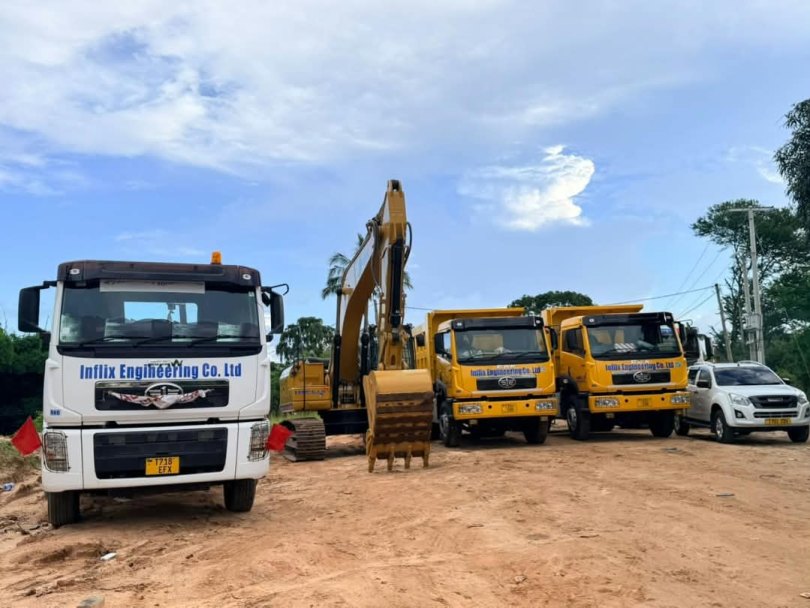 Three Inflix Engineering Co. Ltd FAW tipper trucks and a Caterpillar excavator on a red-earth construction site in Tanzania